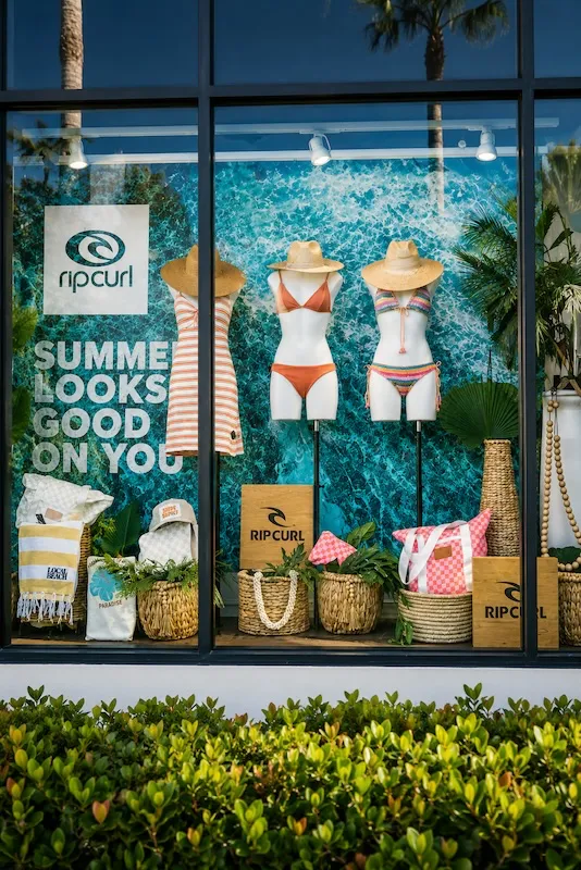 California surf shop window display featuring swimwear, woven beach accessories, and coastal-inspired summer fashion.