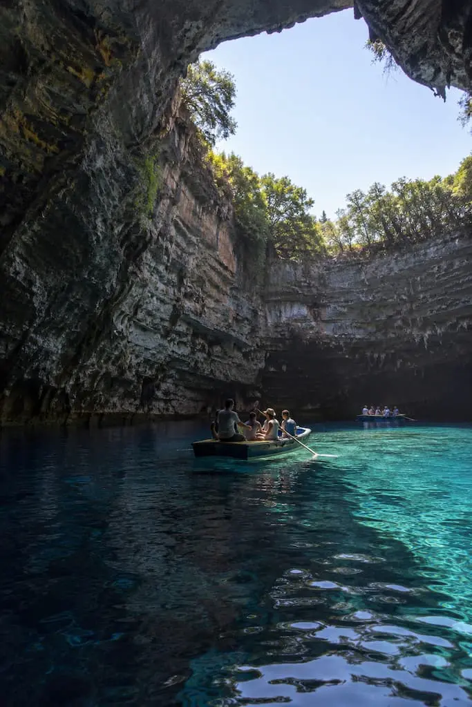 Small rowing boats on a turquoise cave lake beneath a large opening in the limestone roof. Melissani Lake, Kefalonia.