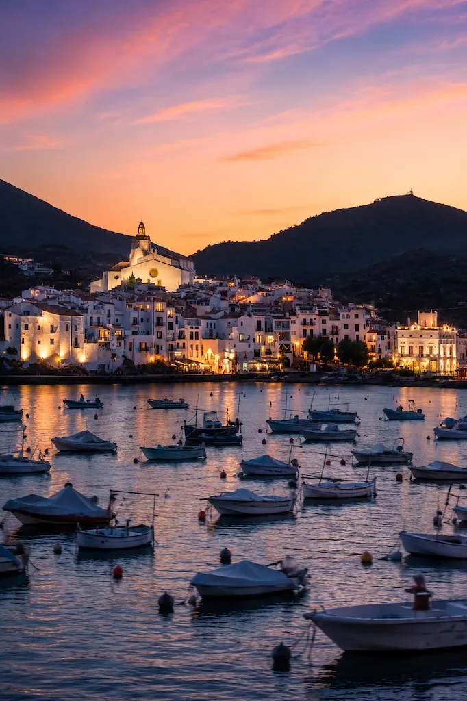 Sunset over the whitewashed harbor of Cadaqués on Spain's Costa Brava with fishing boats and the Mediterranean Sea.