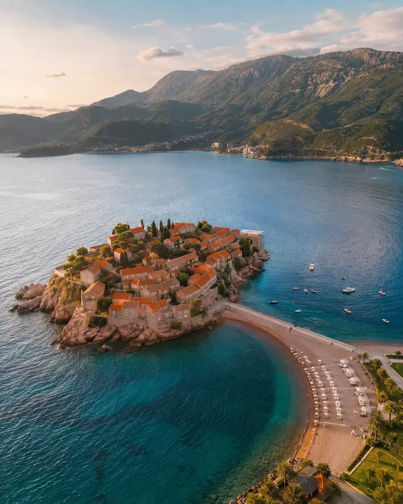 Aerial view of Sveti Stefan, Montenegro, showing the historic stone island village connected to the mainland by a narrow causeway and surrounded by the turquoise Adriatic Sea.