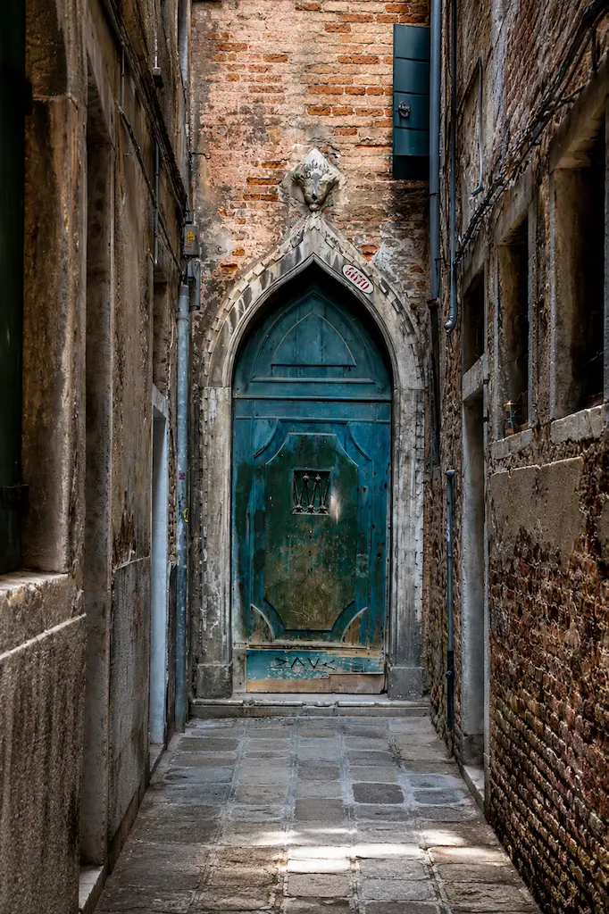 The famous weathered blue door in Venice's Castello district tucked away in a narrow historic alleyway.
