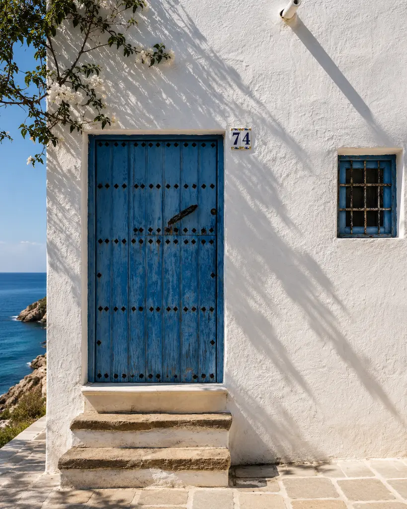 Weathered blue wooden door set into a whitewashed coastal house overlooking the Mediterranean Sea.