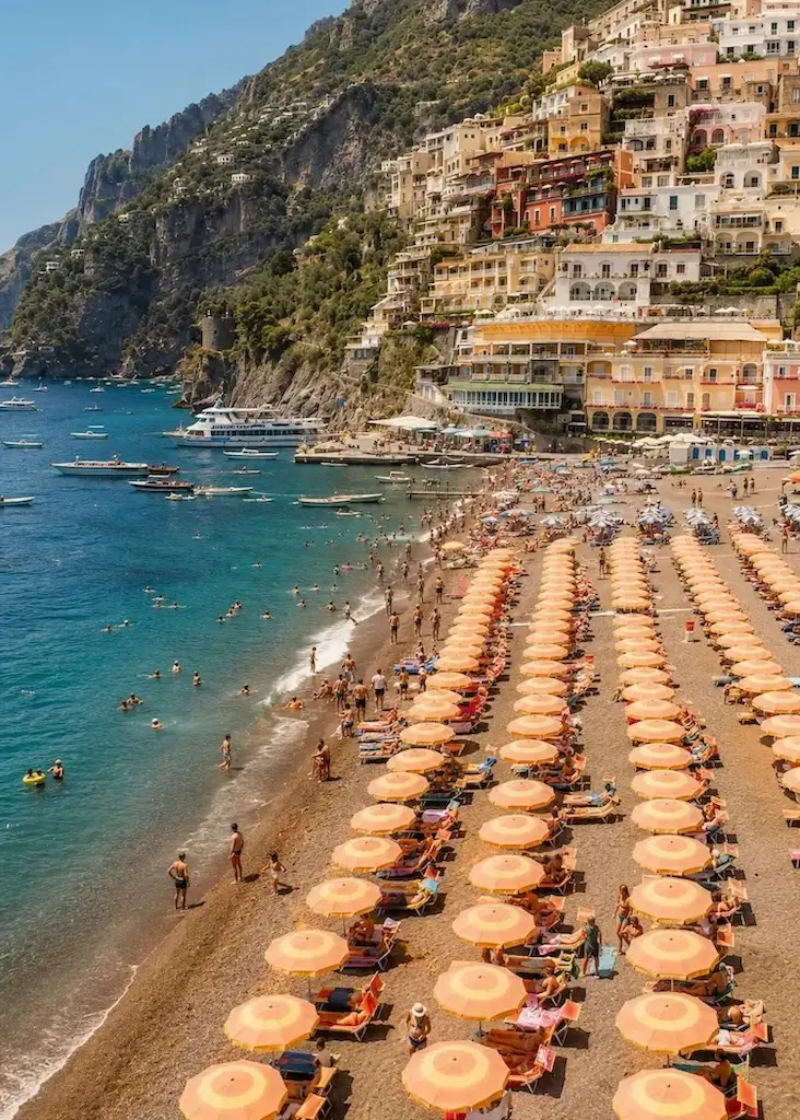 Beach clubs and colorful umbrellas line the beach below the cliffside village of Positano on Italy's Amalfi Coast.