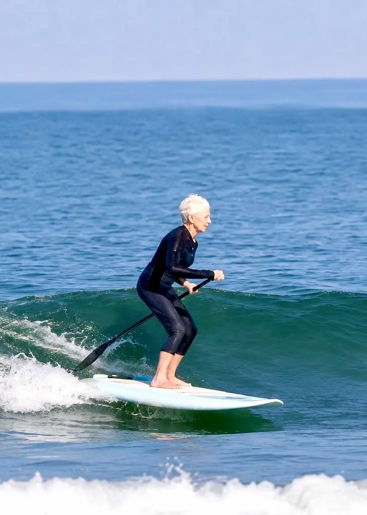 Linda Benson rides a wave standing on a paddleboard, holding a paddle in the Pacific Ocean.