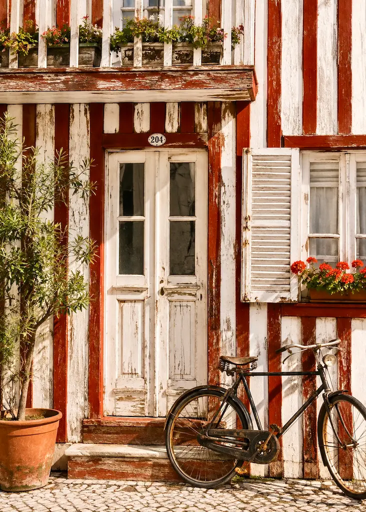 Close view of a traditional red-and-white striped wooden palheiro with shutters and a bicycle in Costa Nova.