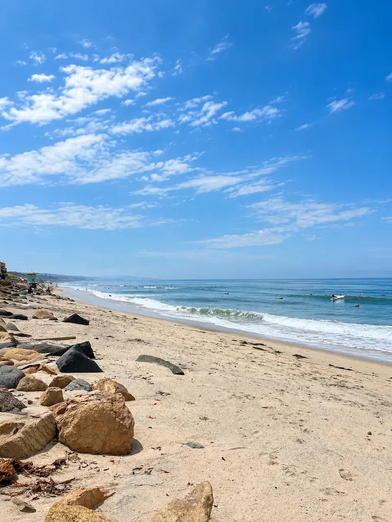 Wide sandy beach in Southern California with surfers, Pacific waves, and plenty of open space along the coastline.