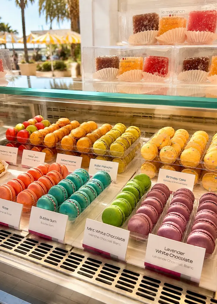 Colorful French macarons displayed in a sunny pâtisserie alongside traditional French confectionery.