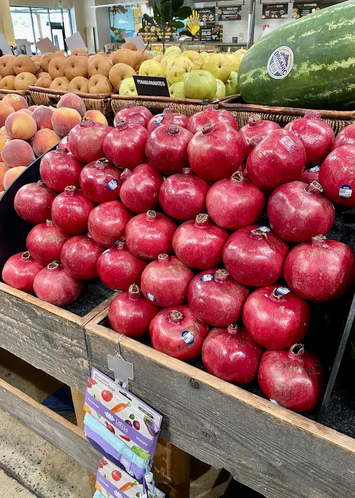 Fresh red pomegranates piled high at a California produce market alongside late-summer fruit.