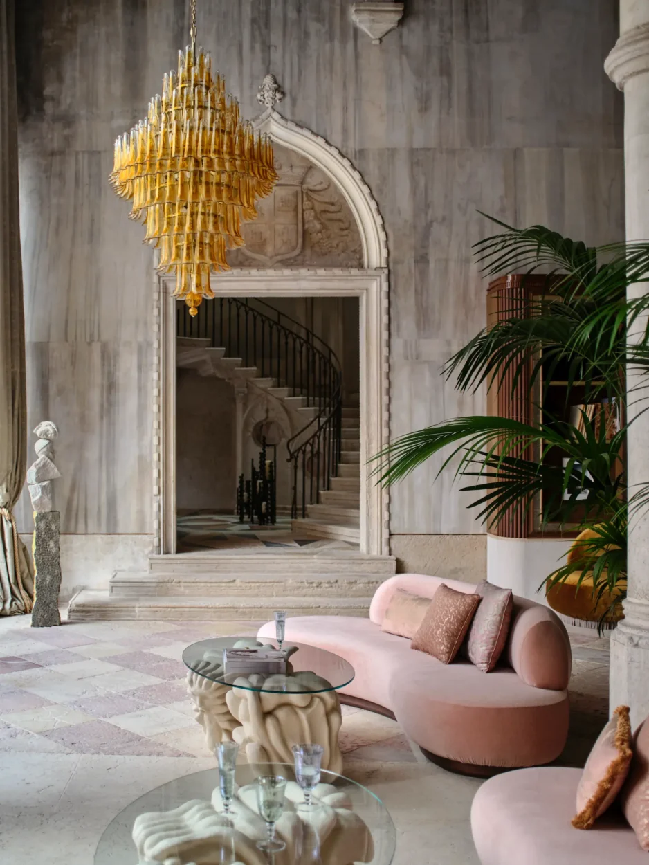 Contemporary seating beneath a Murano chandelier at Orient Express Venezia, with the historic staircase visible through the doorway.