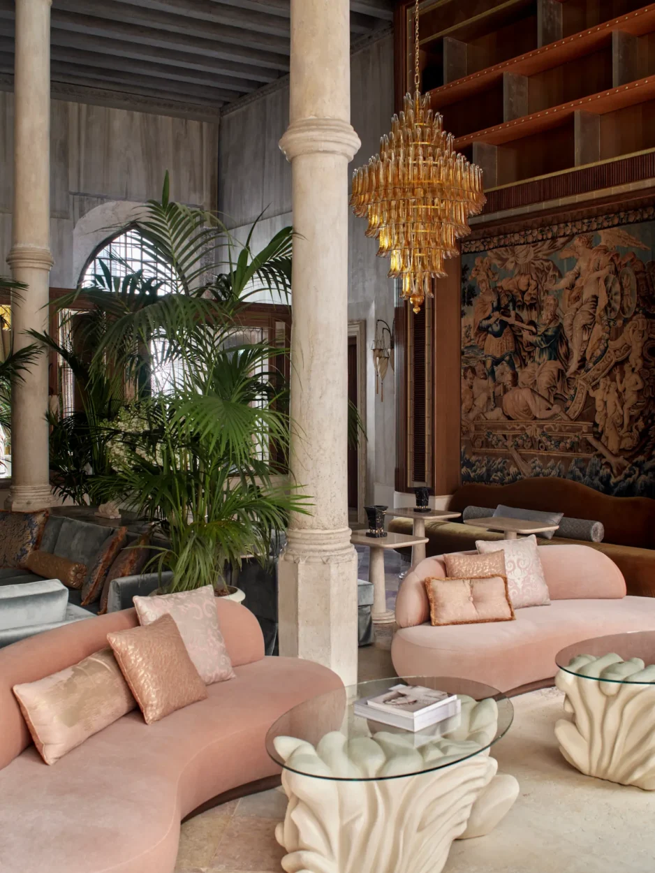Grand lobby at Orient Express Venezia with historic columns, a large tapestry, Murano glass chandelier and contemporary pink seating.