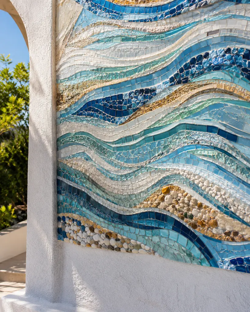 Contemporary coastal wall mosaic made from blue, aqua, white and gold glass tesserae arranged in flowing wave patterns.