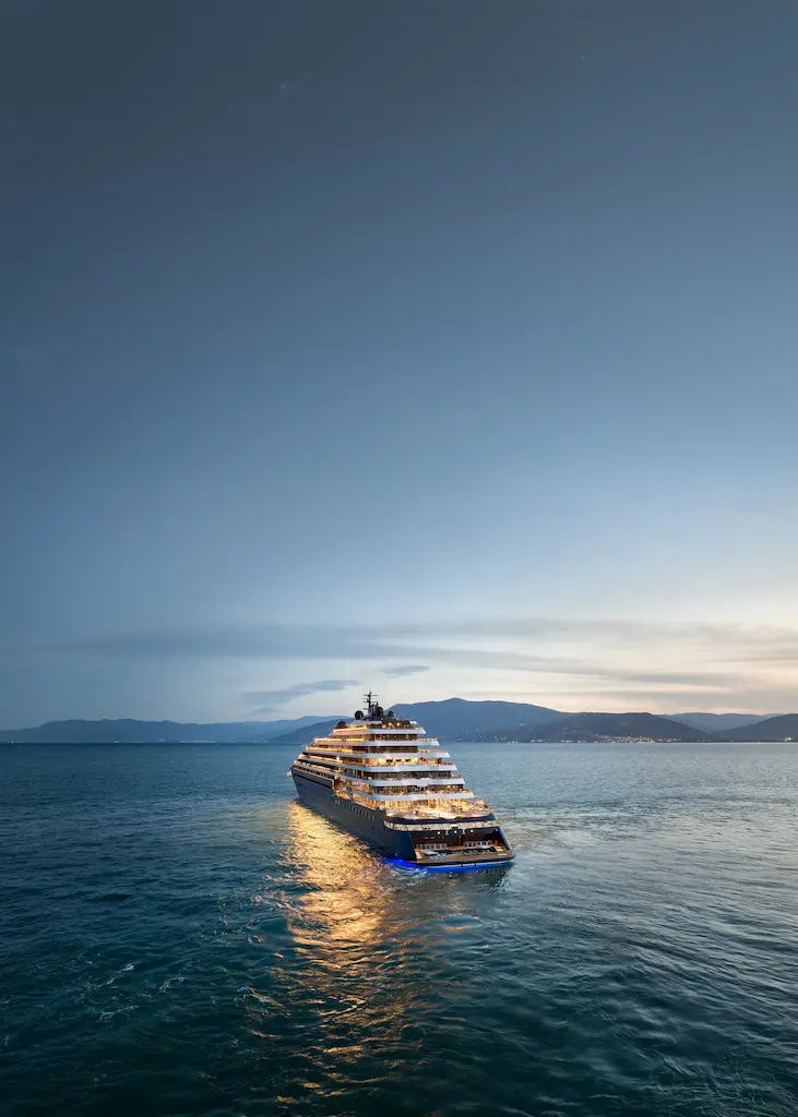 Evrima from The Ritz-Carlton Yacht Collection sailing across calm water at dusk.