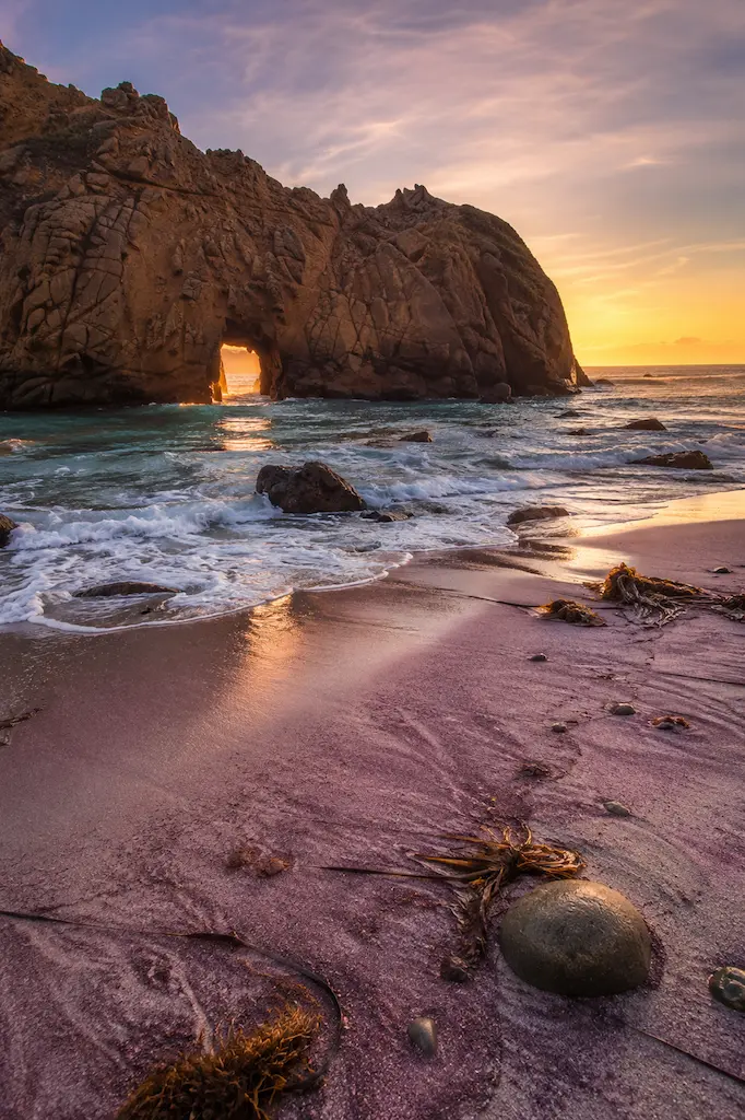 Keyhole Arch at Pfeiffer Beach in late-afternoon light with waves washing across purple-toned sand